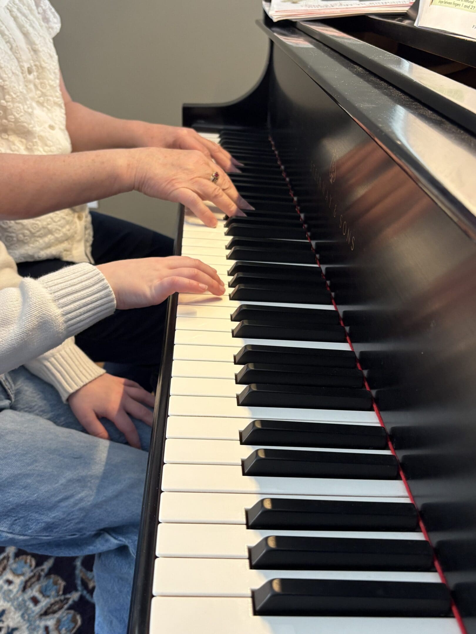 Two people playing piano together, hands on keys.