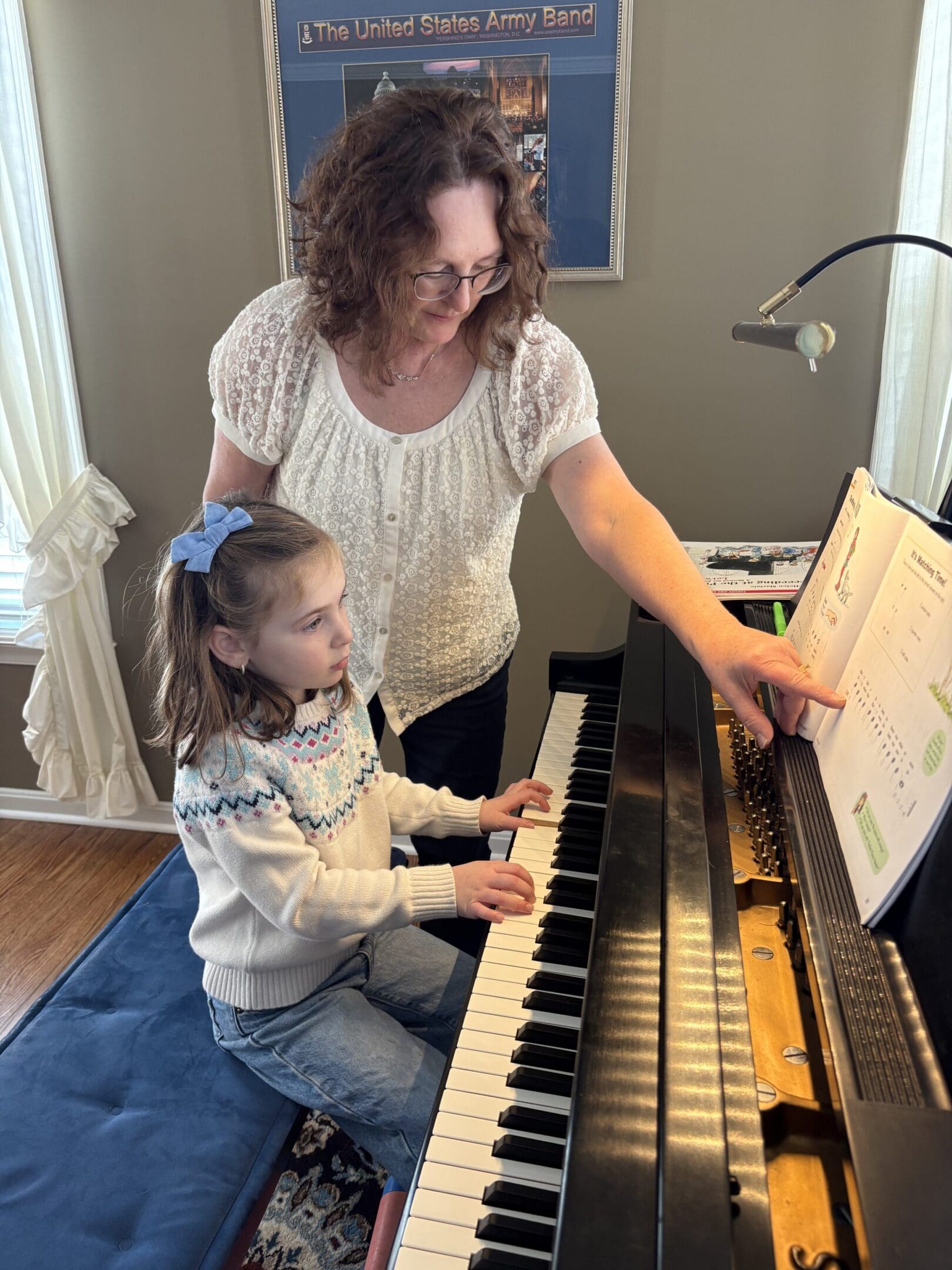 A woman teaching a young girl to play the piano.