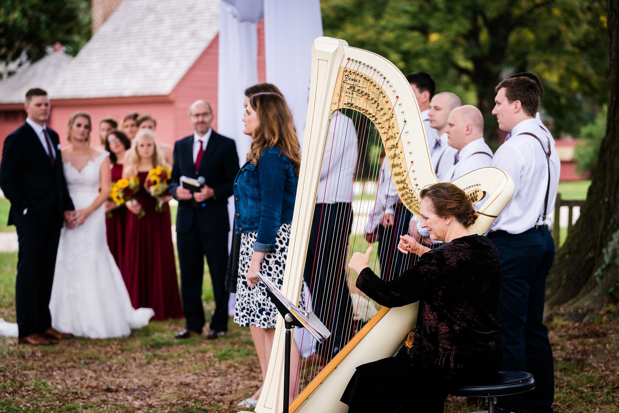 Harpist performs at an outdoor wedding ceremony with guests attentively watching.