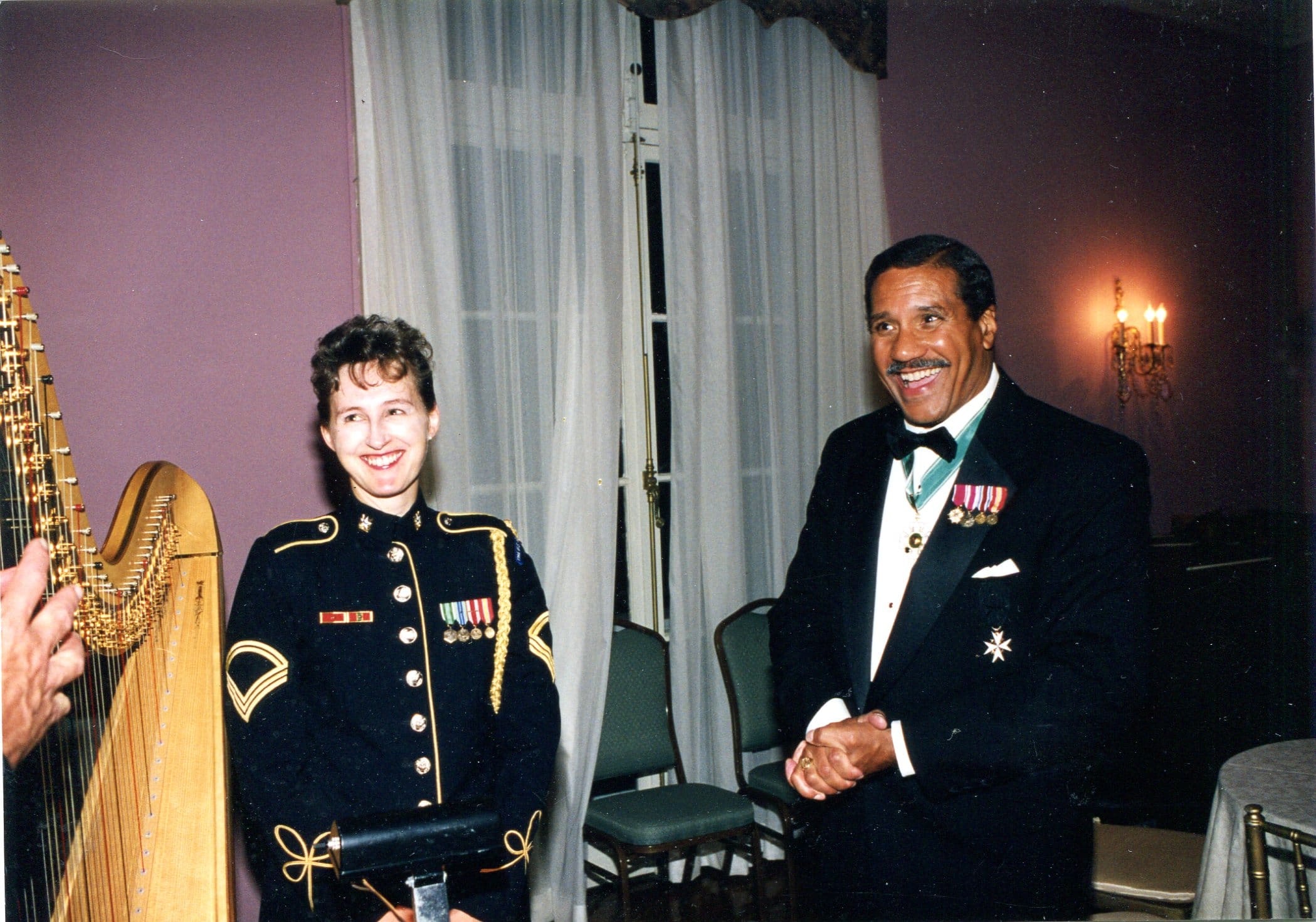 Two people dressed formally, smiling indoors.